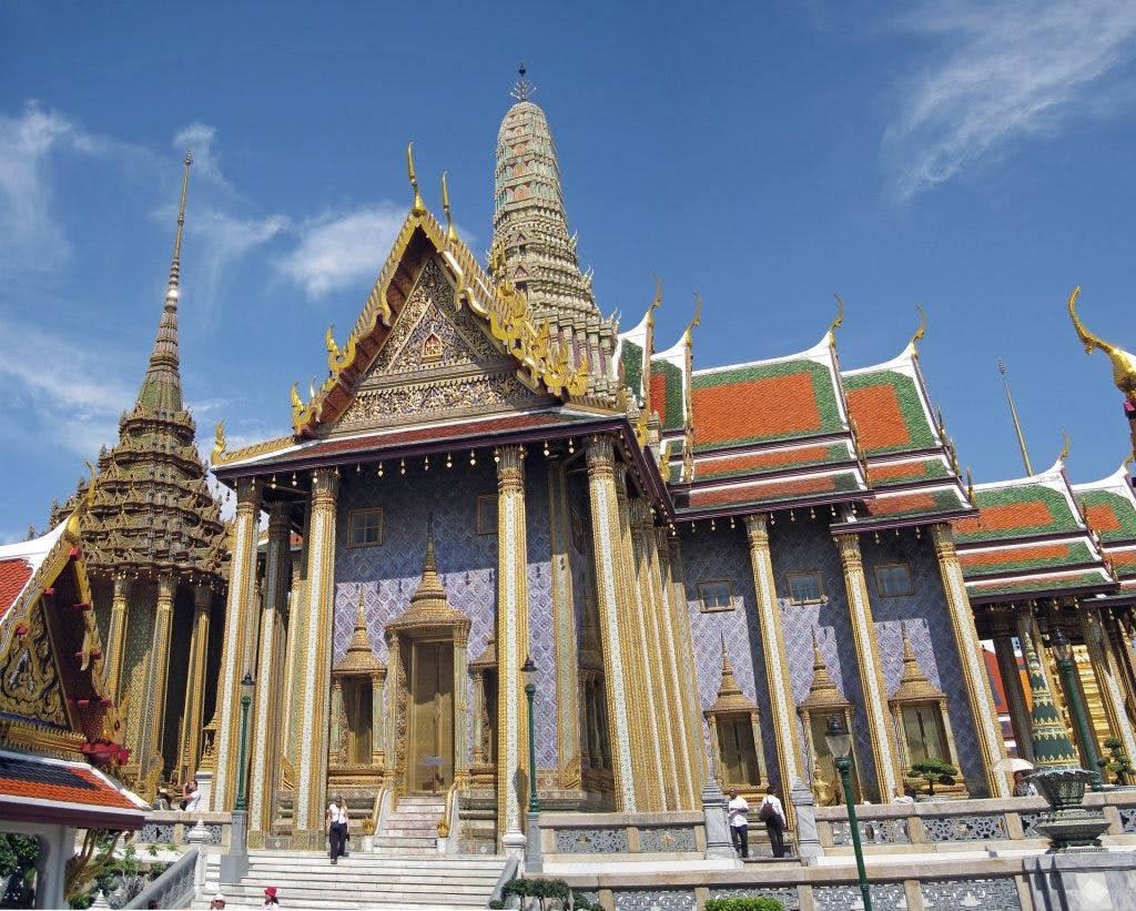 Ornate temple with colorful tiled roofs, intricate carvings, and tall spires under a clear blue sky. Few people at the entrance.