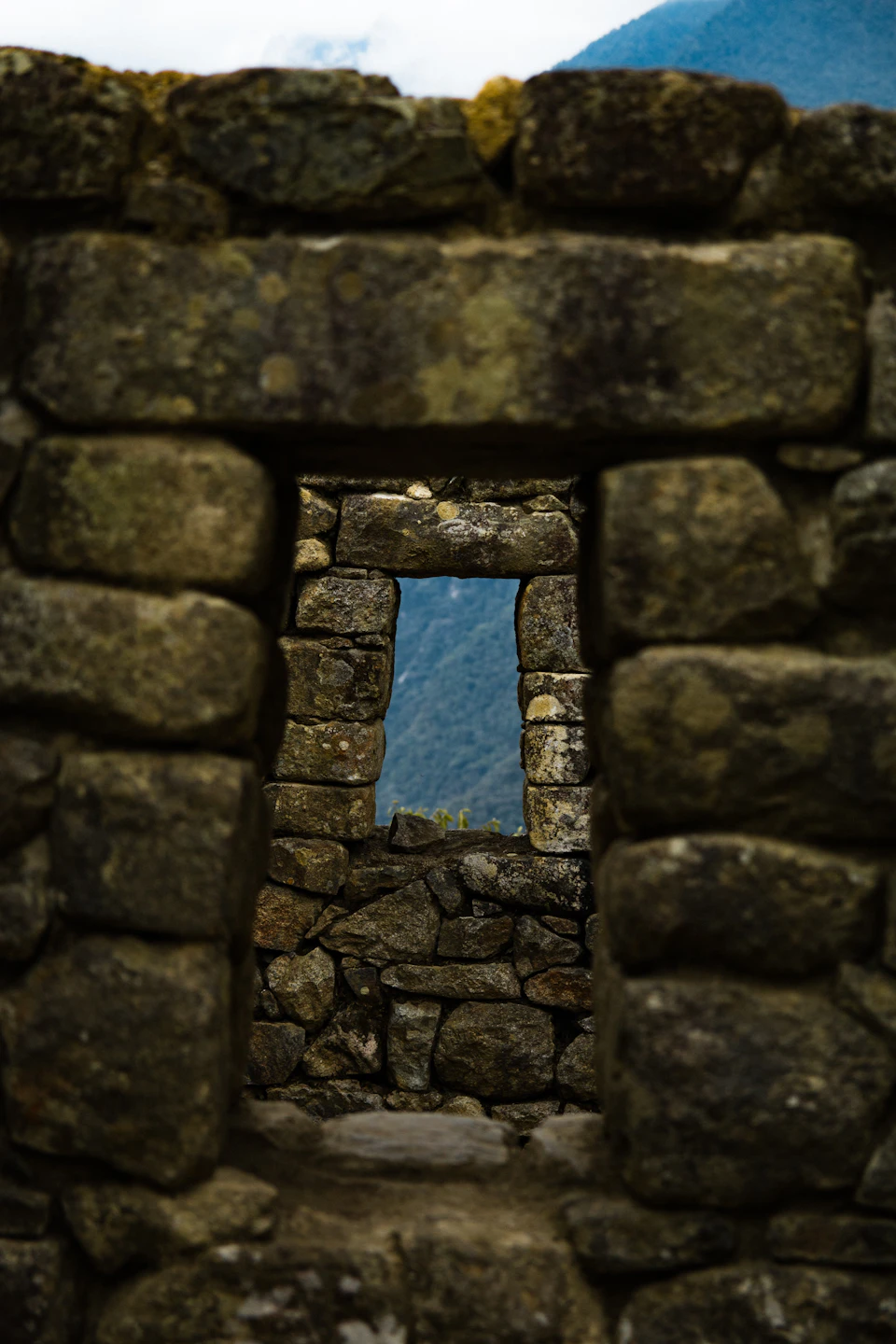 Stony ruins with a rectangular window view of distant mountains and greenery.