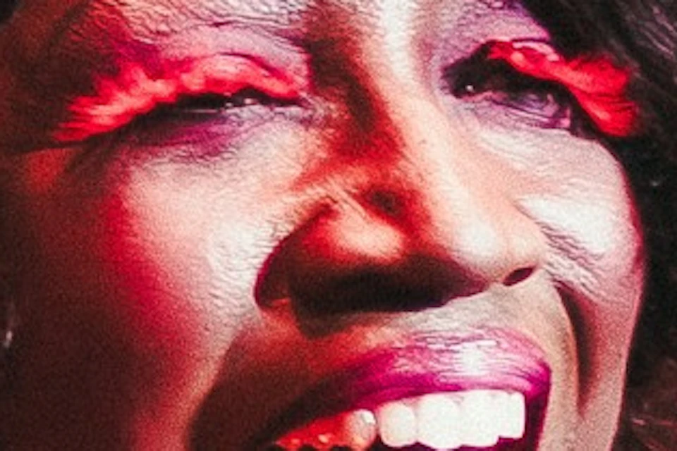 A person in a sequined red outfit smiling widely under stage lighting.