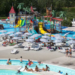 Utomhusvattenpark med pooler, rutschkanor och lekstrukturer. Folk kopplar av under paraplyer och barn leker i vattnet.