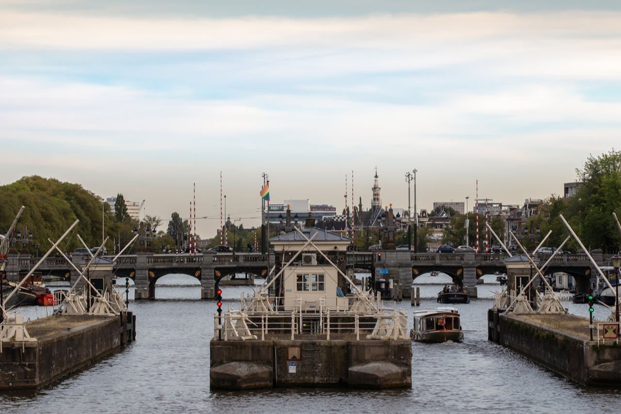 Eine Kanalszene mit Brücken und Anlegestellen, Booten im Wasser und Gebäuden im Hintergrund unter einem teilweise bewölkten Himmel.