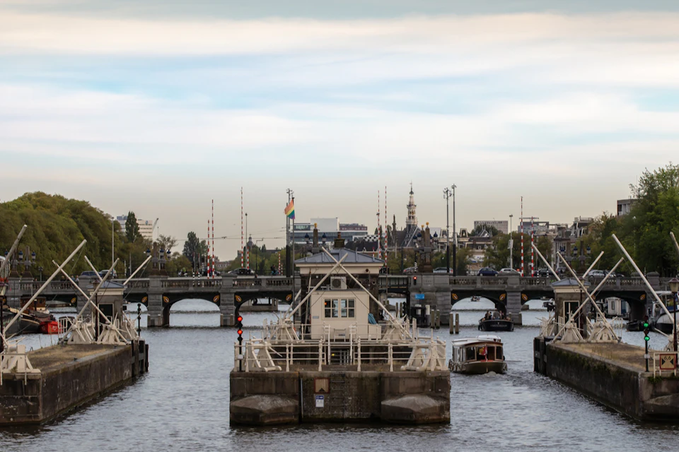 A canal scene with bridges and mooring structures, boats in the water, and buildings in the background under a partly cloudy sky.