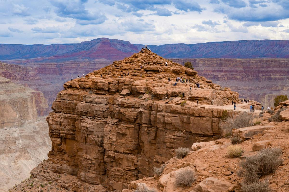 A group of people climbing and exploring a rocky hill at the edge of a canyon under a cloudy sky.