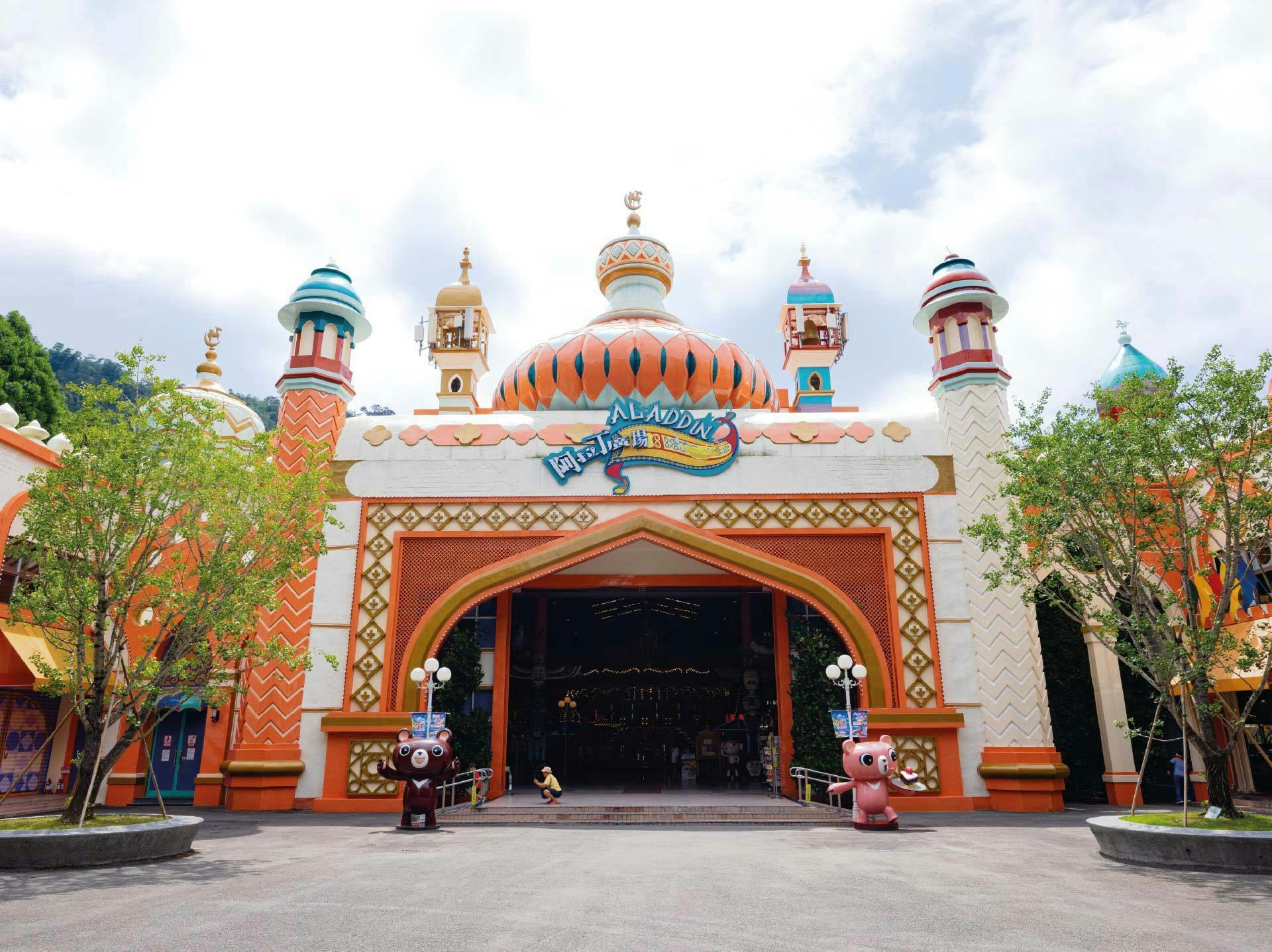 The colorful entrance of an Aladdin-themed attraction with domed towers, decorative details, and cartoon statues.