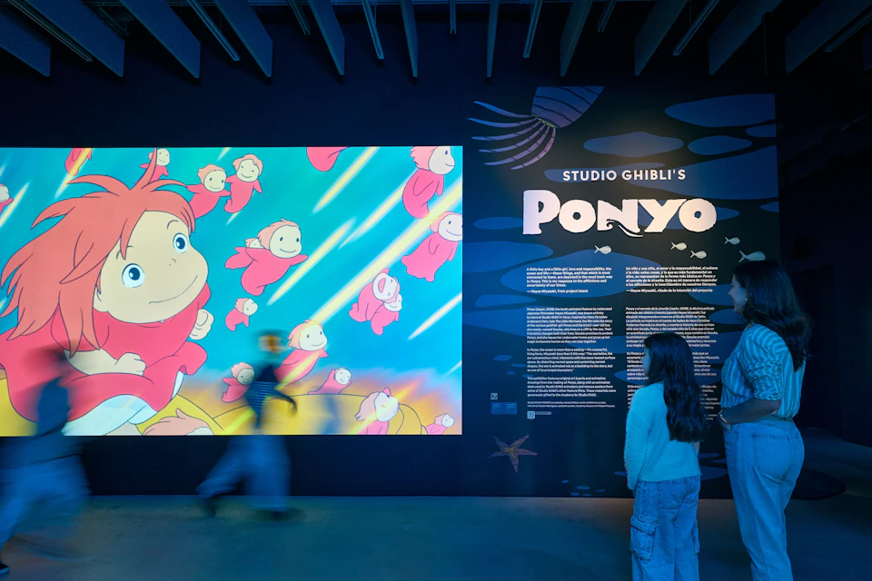 A person observes a colorful display about Studio Ghibli's Ponyo at an exhibition, featuring vibrant artwork and text.