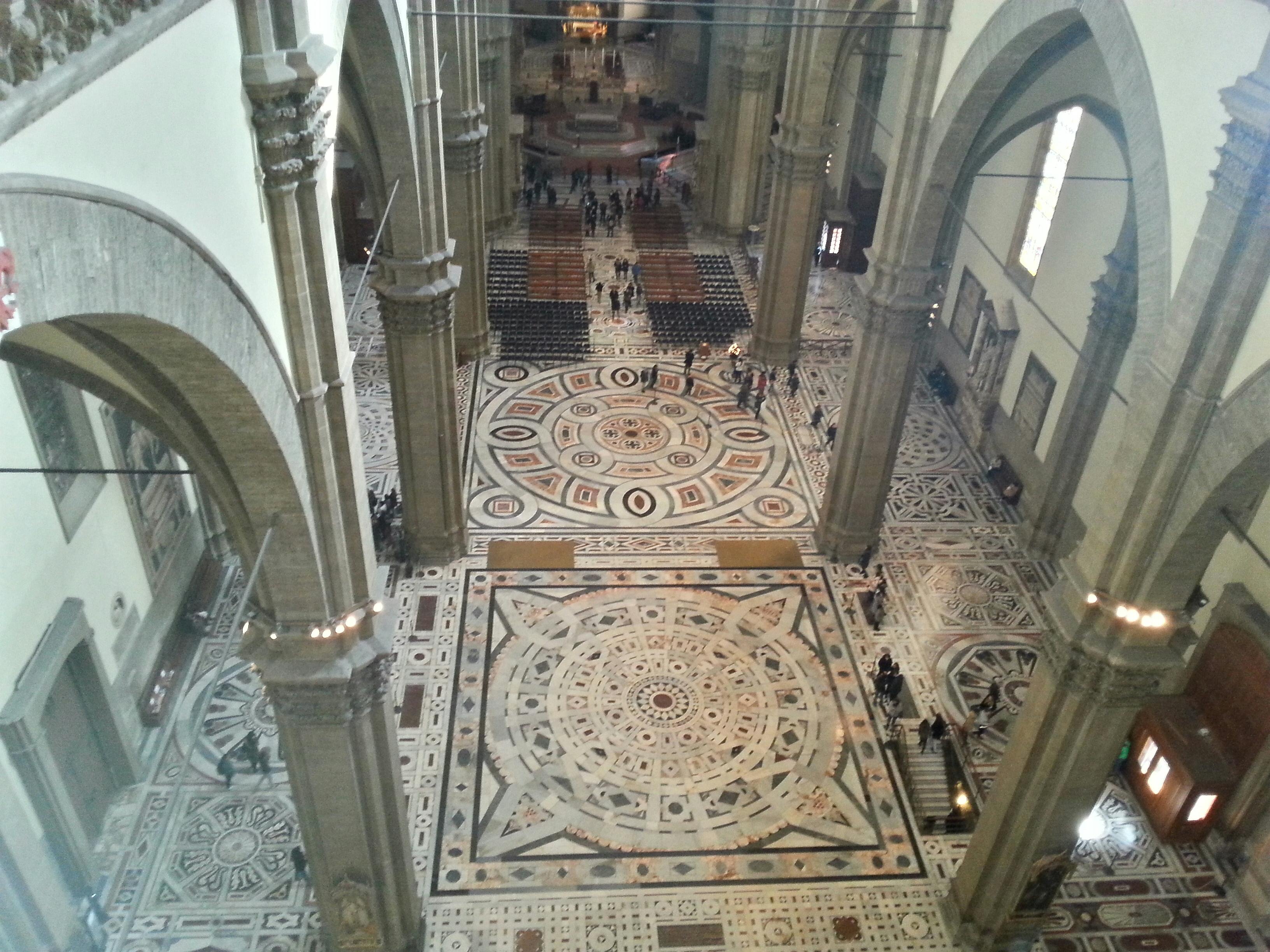 大教堂内部的鸟瞰图，带有错综复杂的图案地砖、高柱和小群人行走。