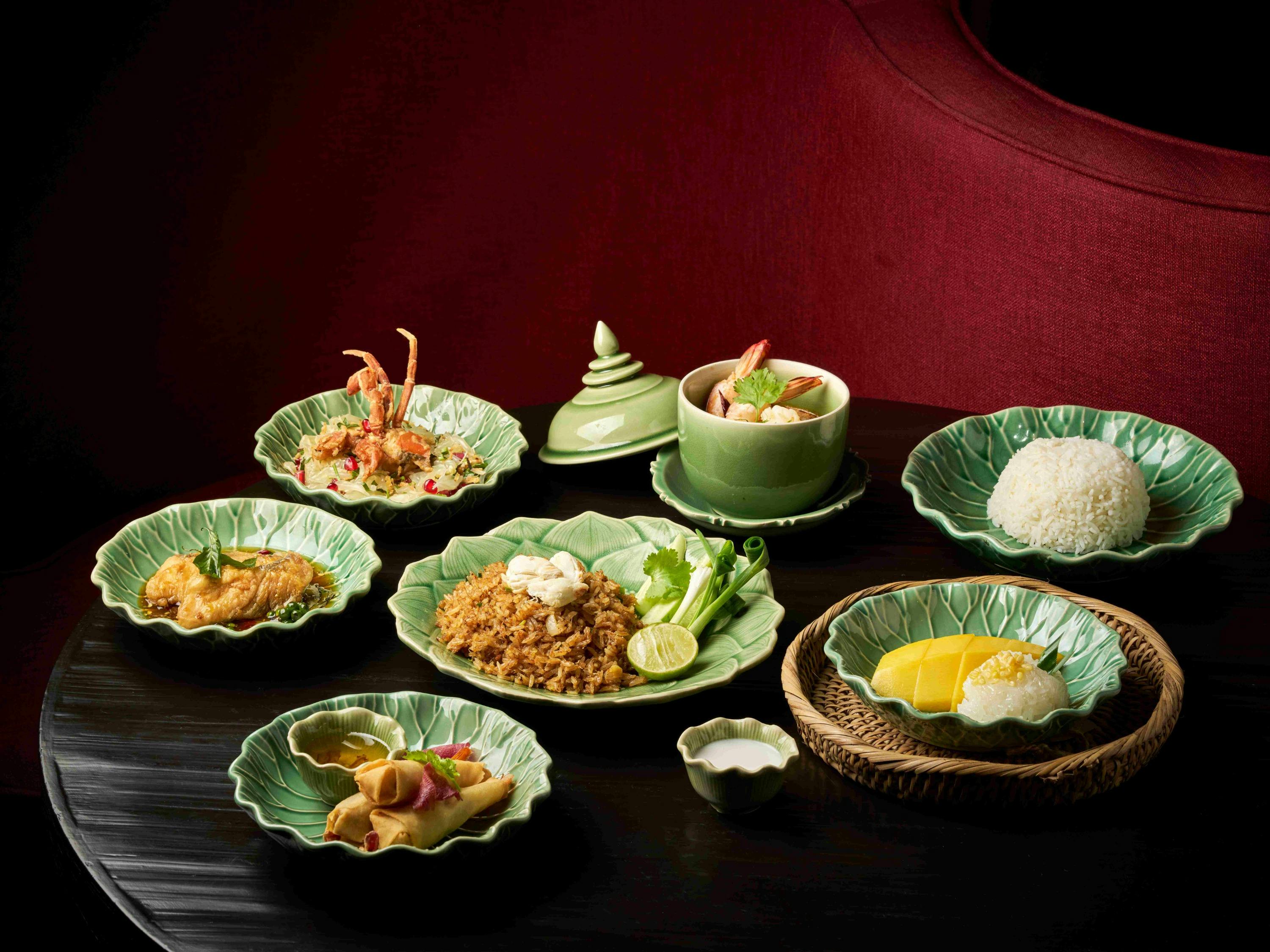 An arrangement of Thai dishes served on green ceramic plates, including rice, mango with sticky rice, curry, and fried rice.