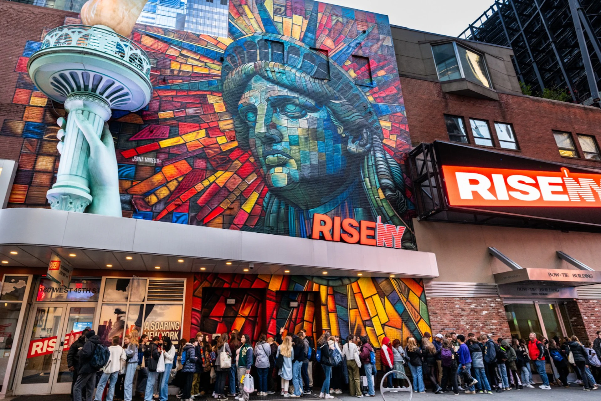 A colorful mural of the Statue of Liberty on a building facade with a crowd of people standing in line below.