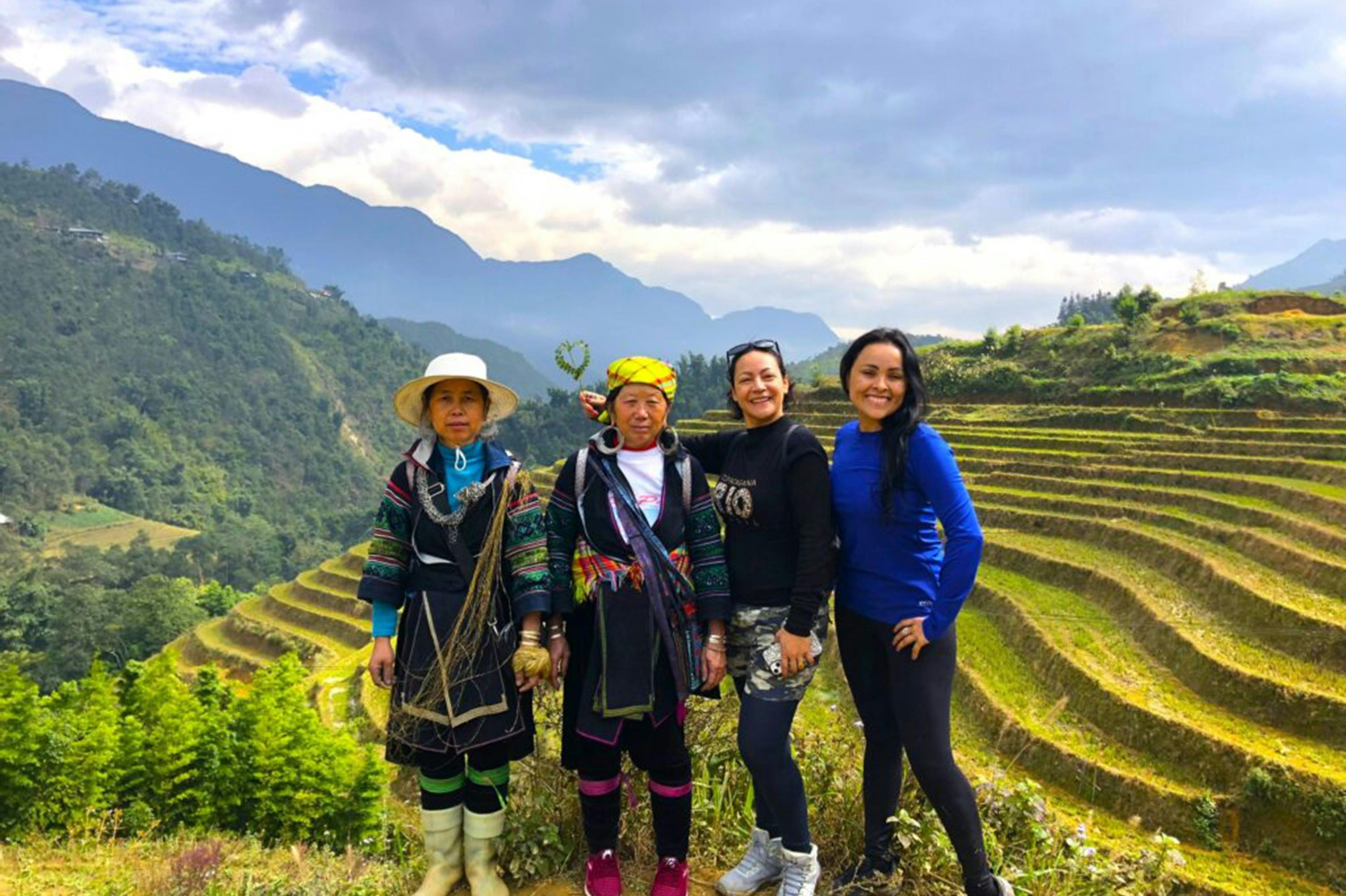흐린 하늘과 푸르고 푸른 언덕을 배경으로 네 명의 여성이 산비탈의 계단식 논 앞에 서 있습니다.