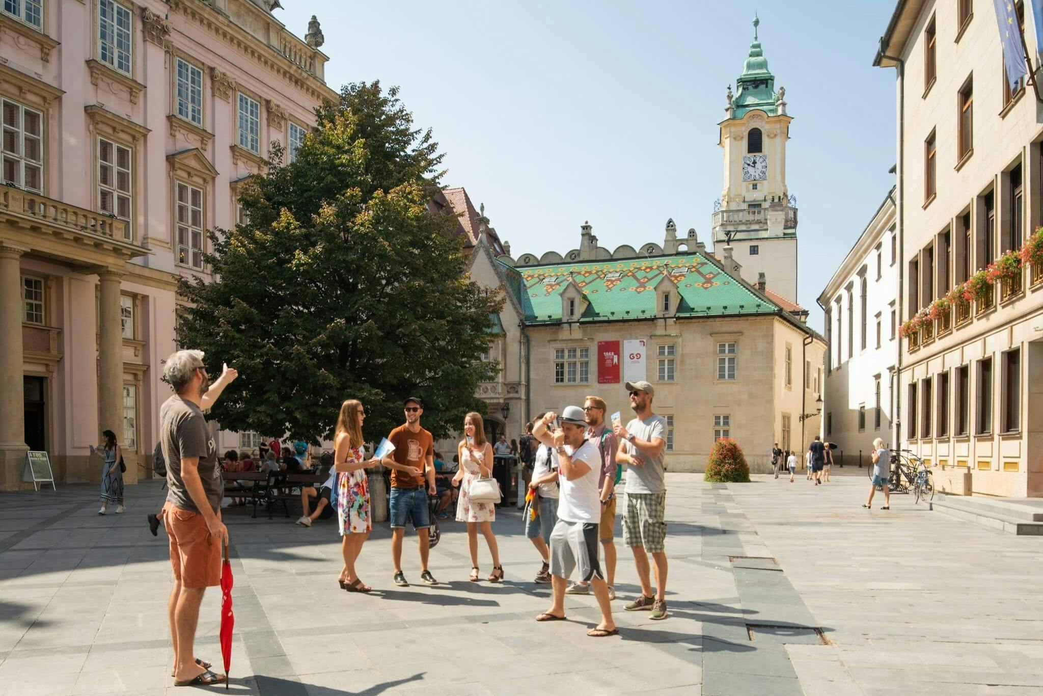 一群人站在一个广场上交谈，广场上有历史建筑，后面有一座钟楼。