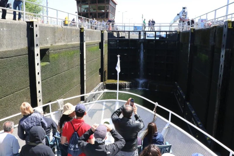 People on the bow of an Argosy boat take photos of the locking chamber, with tall concrete walls on either side