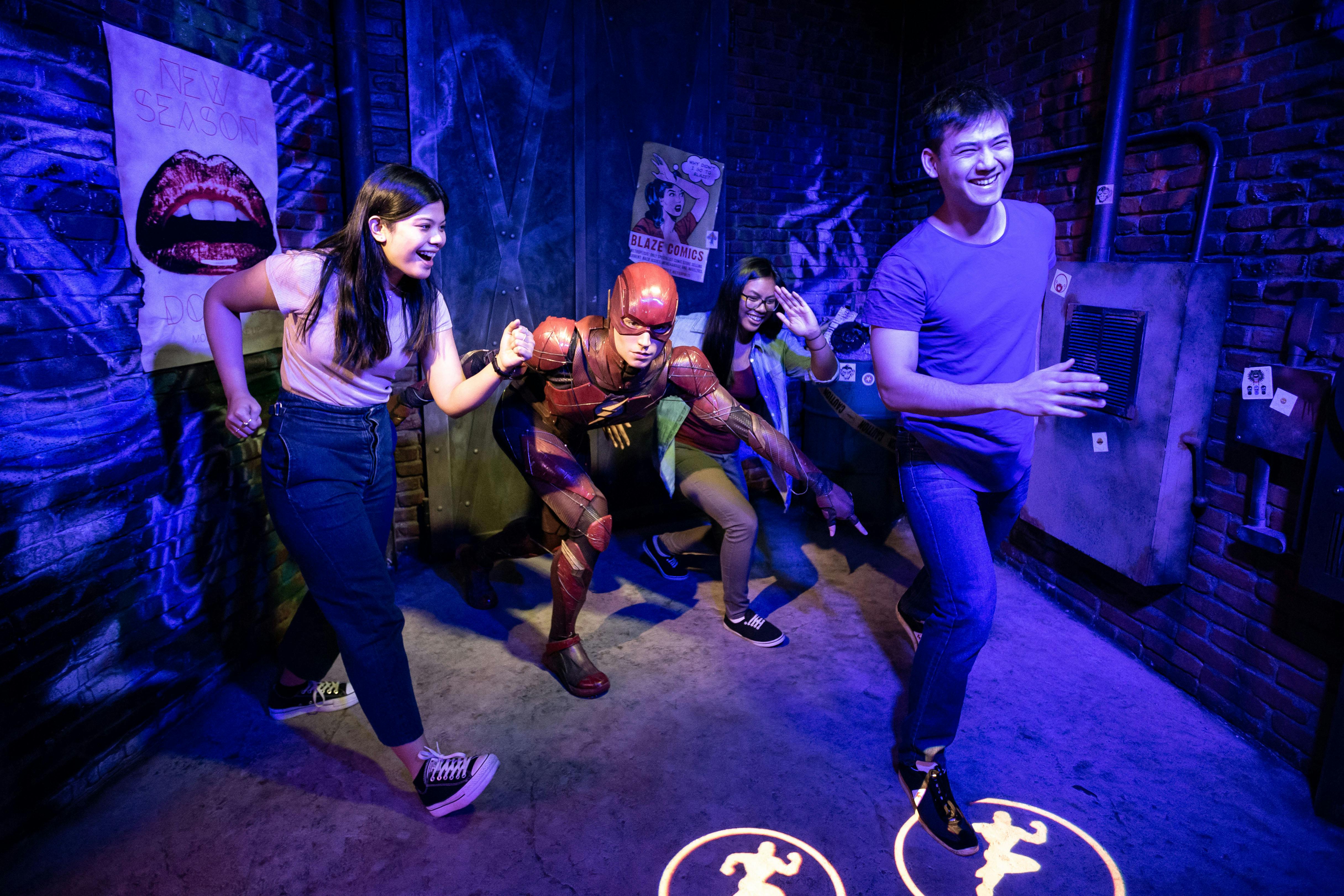 レンガの壁とコミックをテーマにしたポスターが飾られた部屋で、スーパーヒーローのコスチュームを着た人と遊び心溢れるポーズをとっている人々。