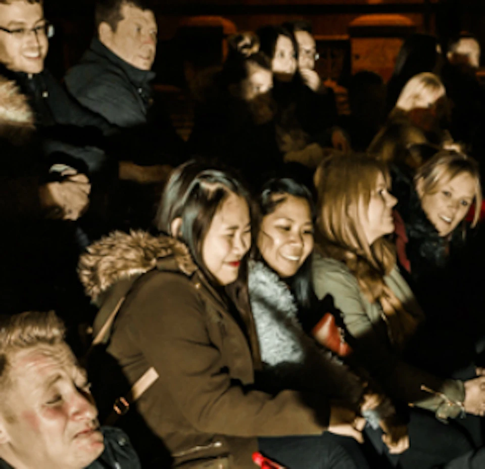 A man in a dark coat performs for a seated audience, holding what appears to be fake organs, while another person stands in the background.