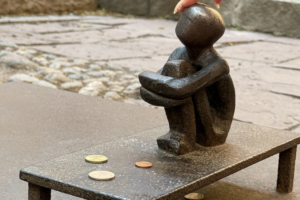 Small bronze sculpture of a person sitting with arms wrapped around knees. Coins are scattered in front on a flat surface.