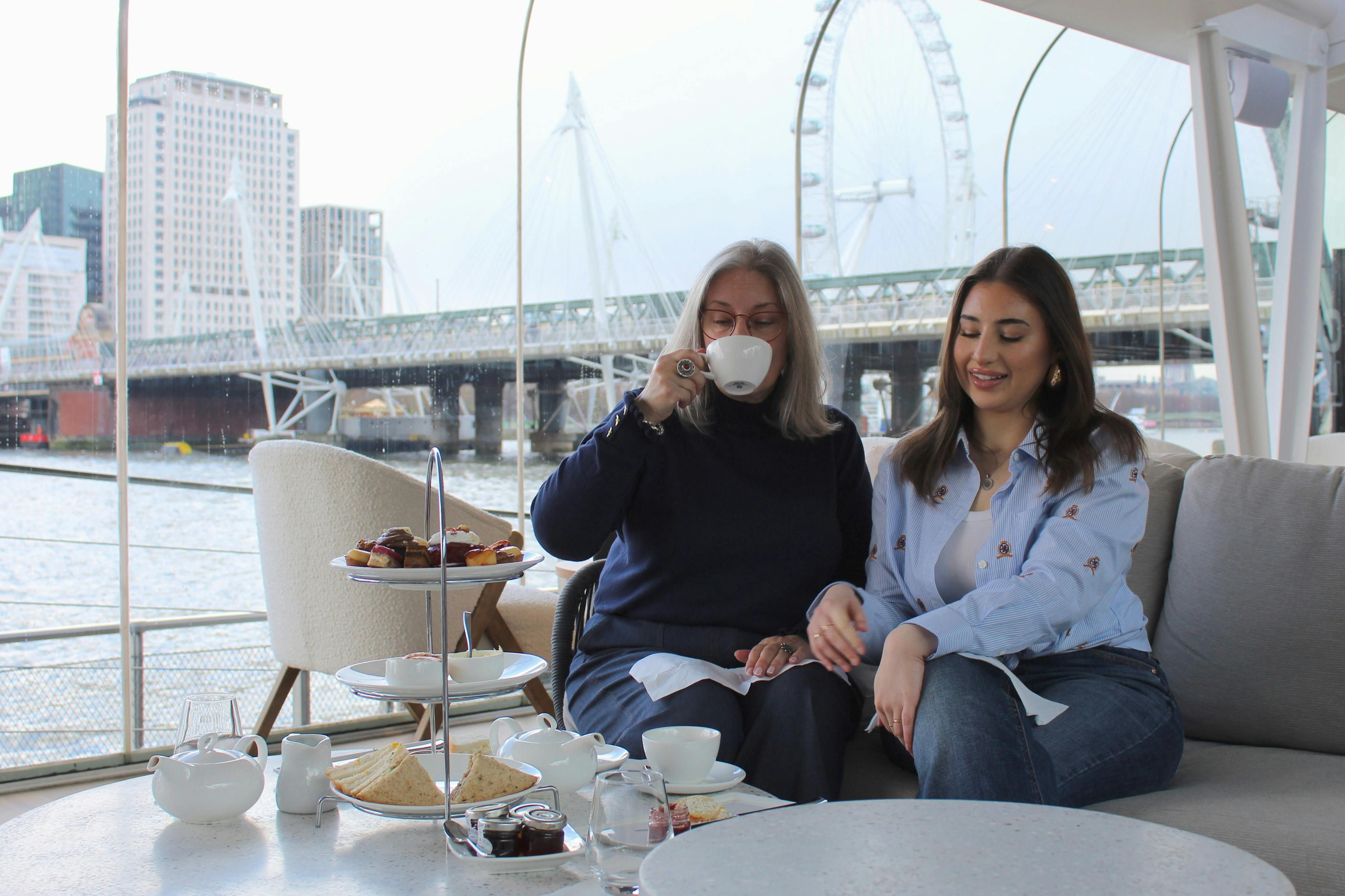 2人の女性がソファに座り、目の前にはロンドン・アイと橋が見えます。