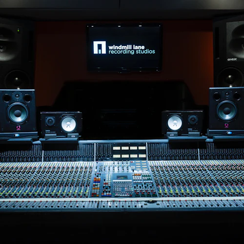 A recording studio control room with a large audio mixing console, multiple speakers, and a screen displaying "windmill lane recording studios."