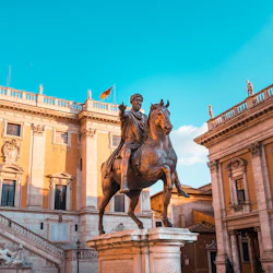 Ryttarstaty framför en historisk byggnad med utsmyckade arkitektoniska detaljer och en klarblå himmel.