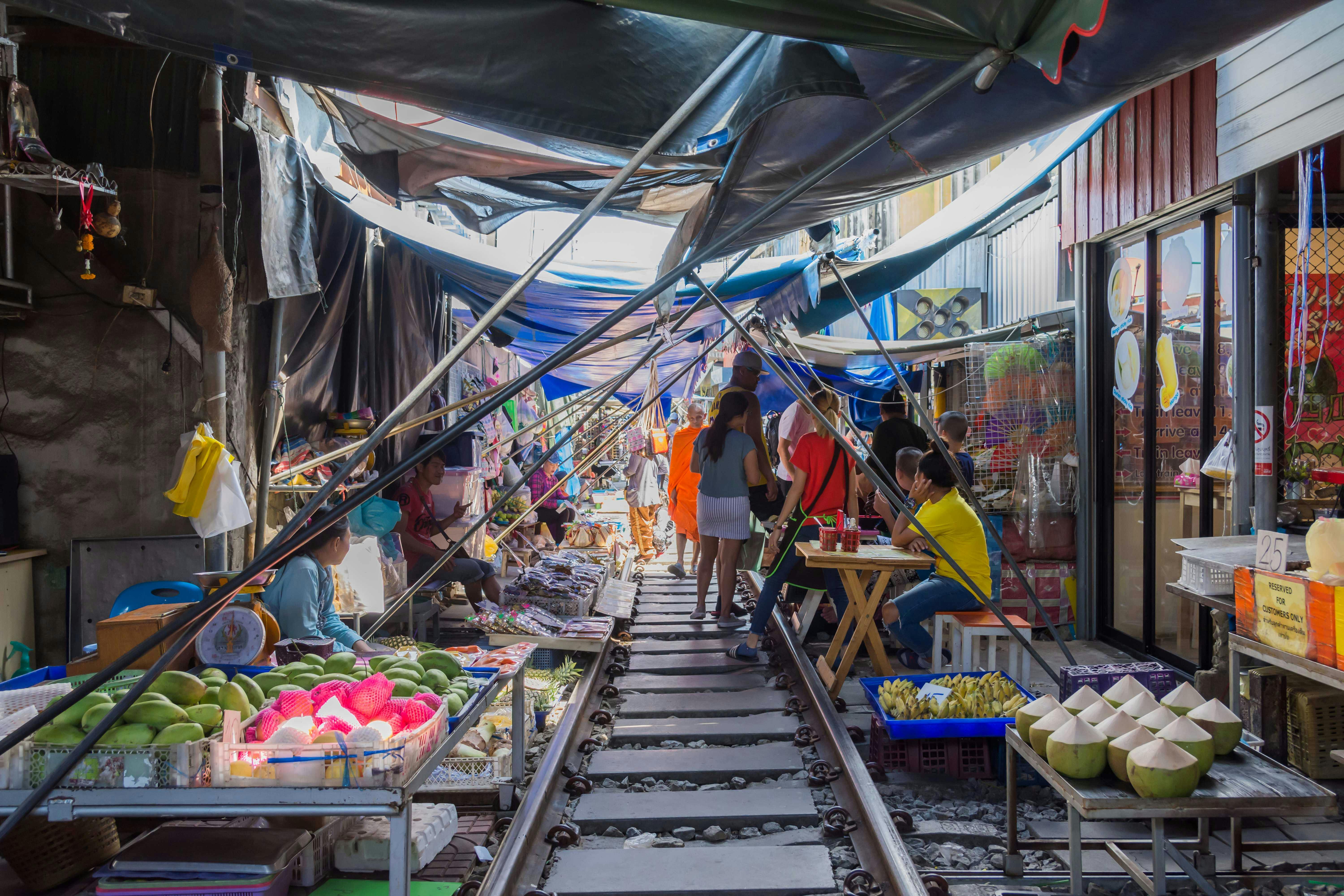 A market set up along train tracks, with vendors selling produce and people walking and shopping under tarps for shade.