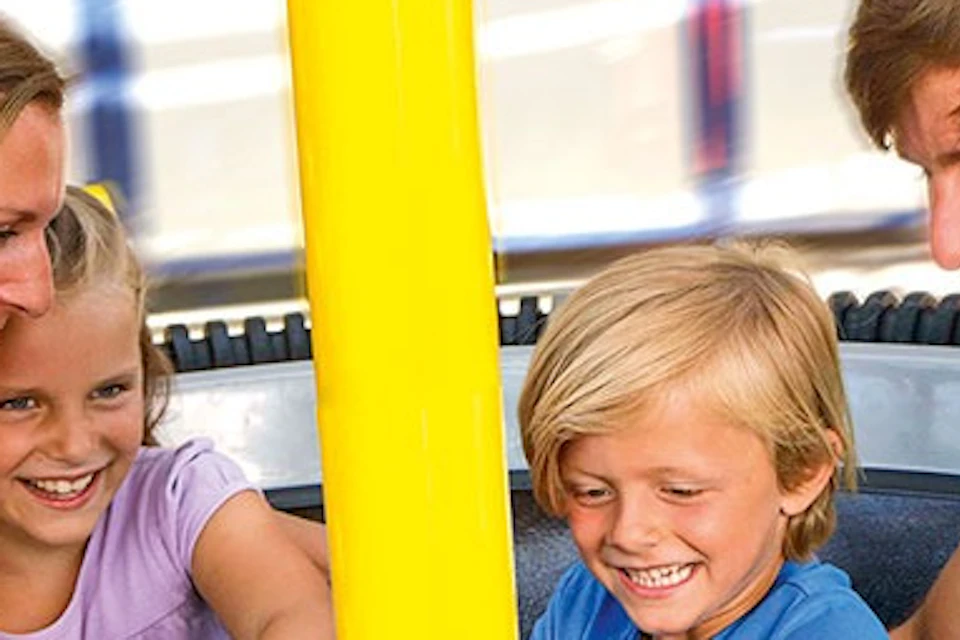 A family of four smiles and laughs while seated on an amusement park ride with a central yellow pole.