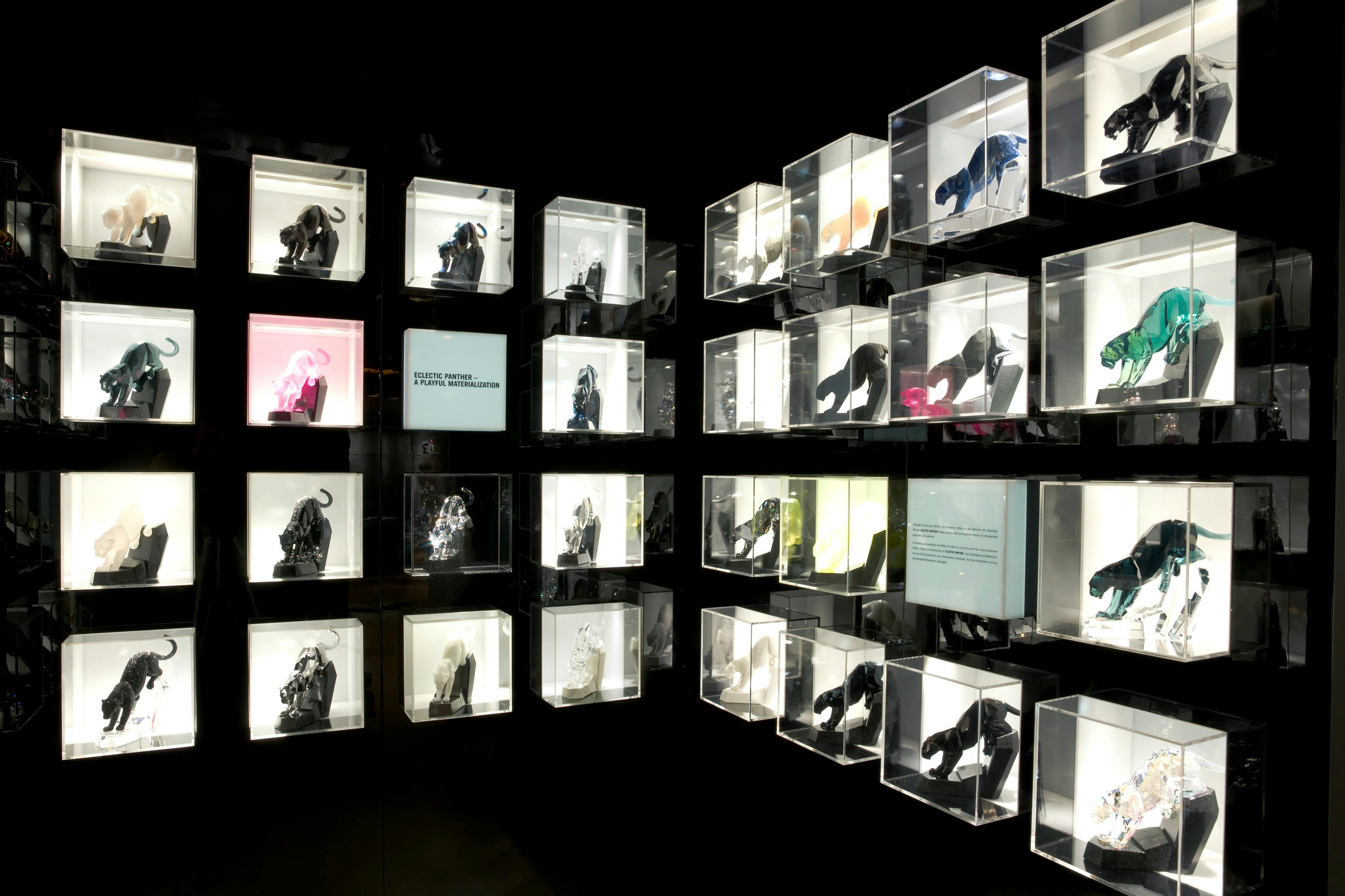 照らされた透明な箱に様々な彫刻が展示され、グリッドパターンで配置された美術展の壁。