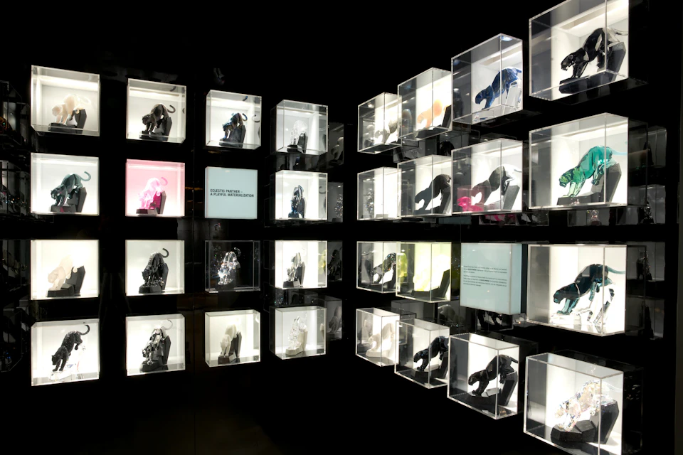 Art exhibition wall with various sculptures displayed in illuminated transparent boxes, arranged in a grid pattern.