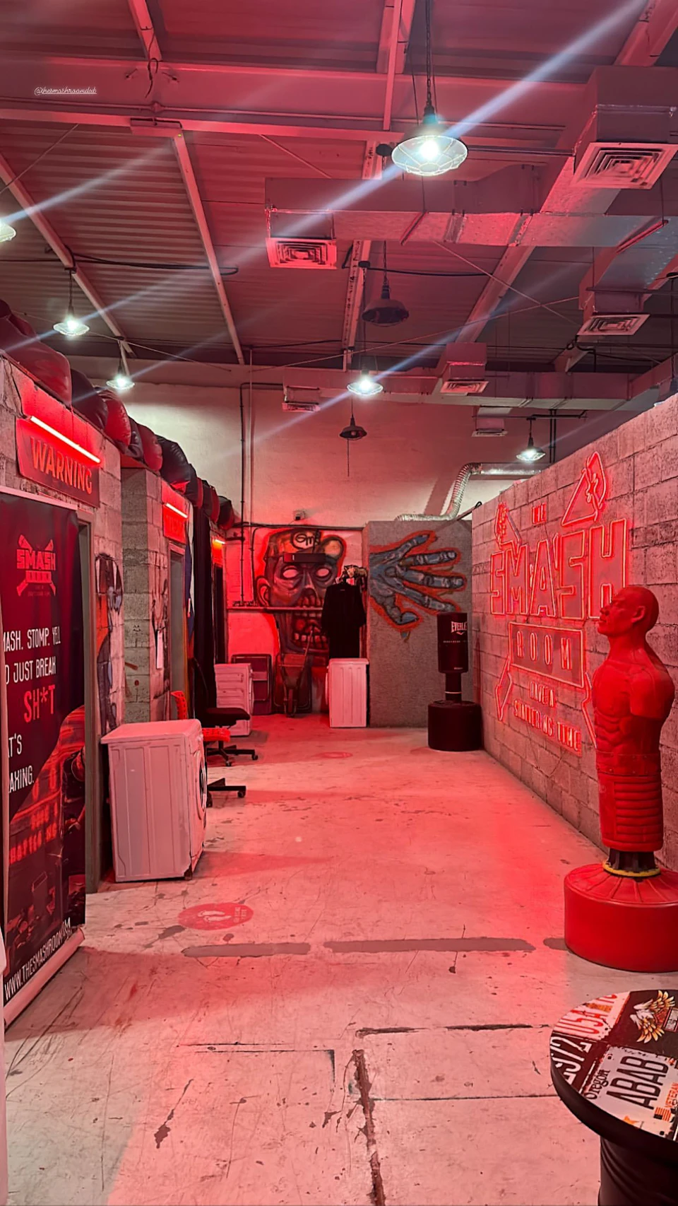A room with red lighting, including punching bags, a mannequin, wall art, and a sign that reads "SMASH ROOM."