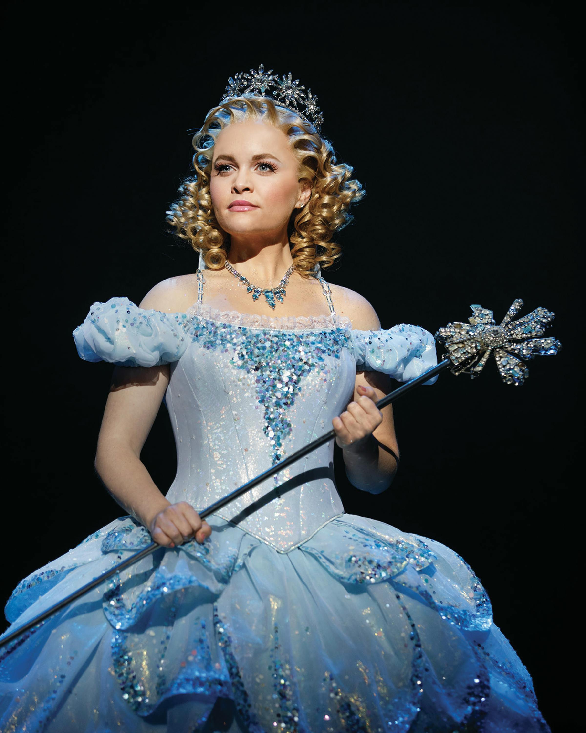 一个人穿着一件精致的浅蓝色长袍，饰有银色细节，戴着皇冠，拿着一根魔杖，末端有一颗星星。