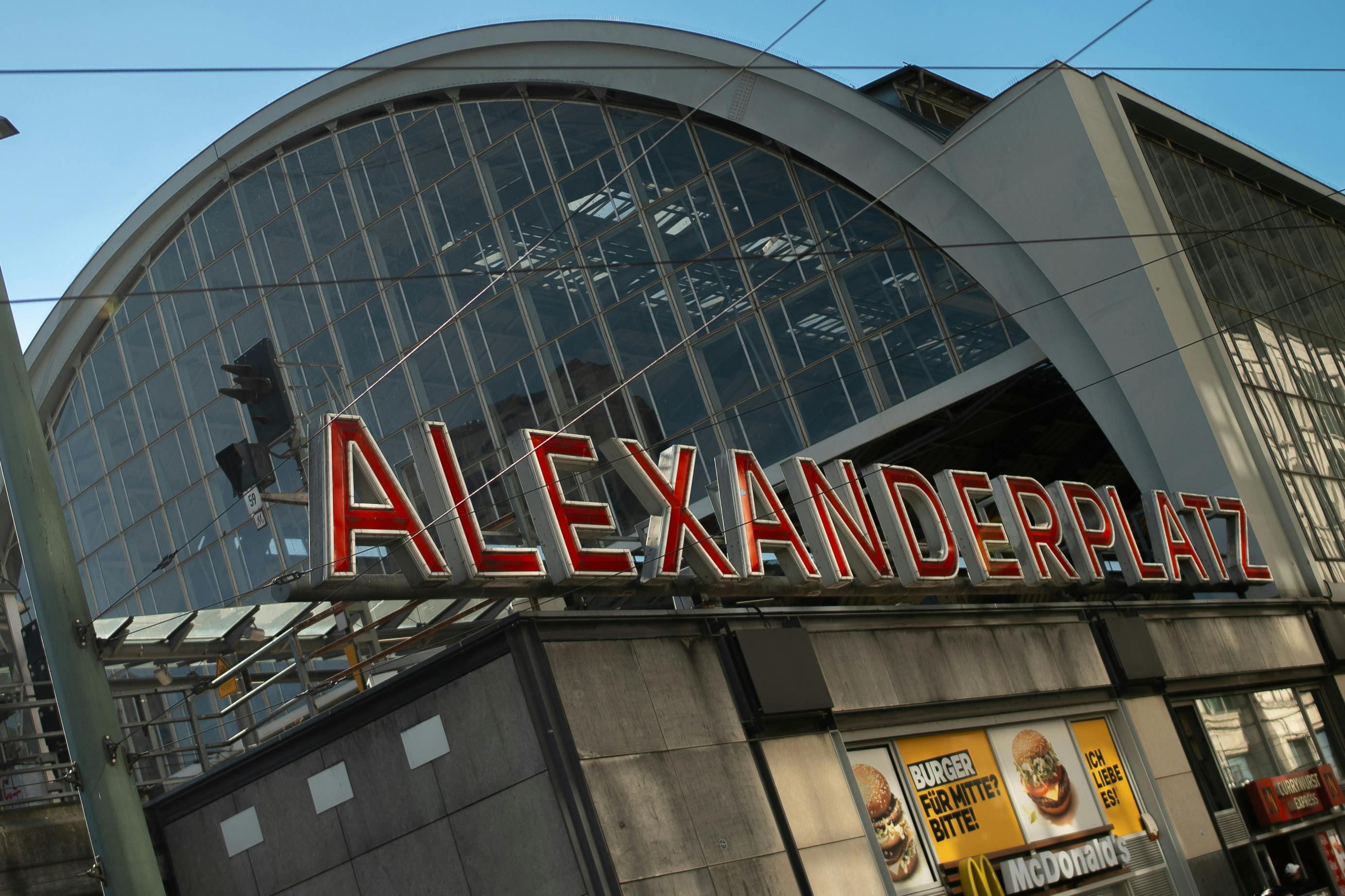 A entrada de um edifício com uma grande placa onde se lê "Alexanderplatz" e um anúncio do McDonald's por baixo.