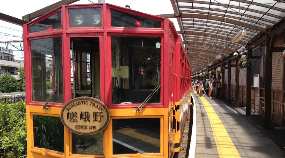 A colorful train labeled "Romantic Train" at a station platform with a roofed structure and passengers waiting nearby.