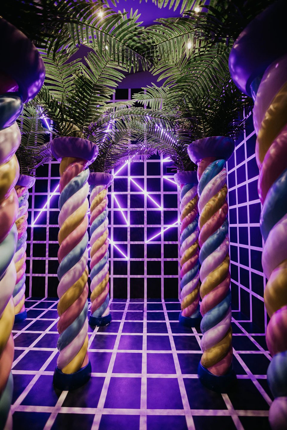 Colorful spiral columns with palm leaves, neon purple geometric lights, and a checkered black-and-white floor and walls.