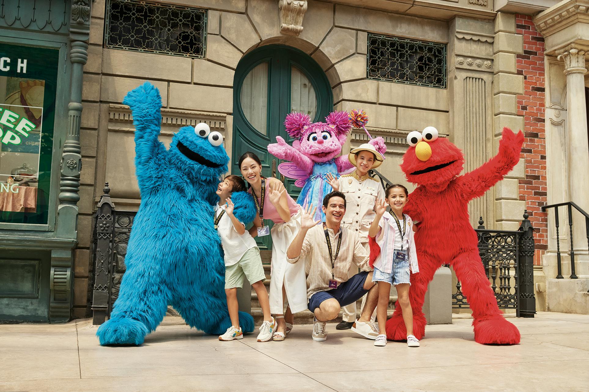 건물 앞에서 쿠키 몬스터, 애비 캐더비, 엘모로 분장한 캐릭터와 포즈를 취하고 있는 가족.