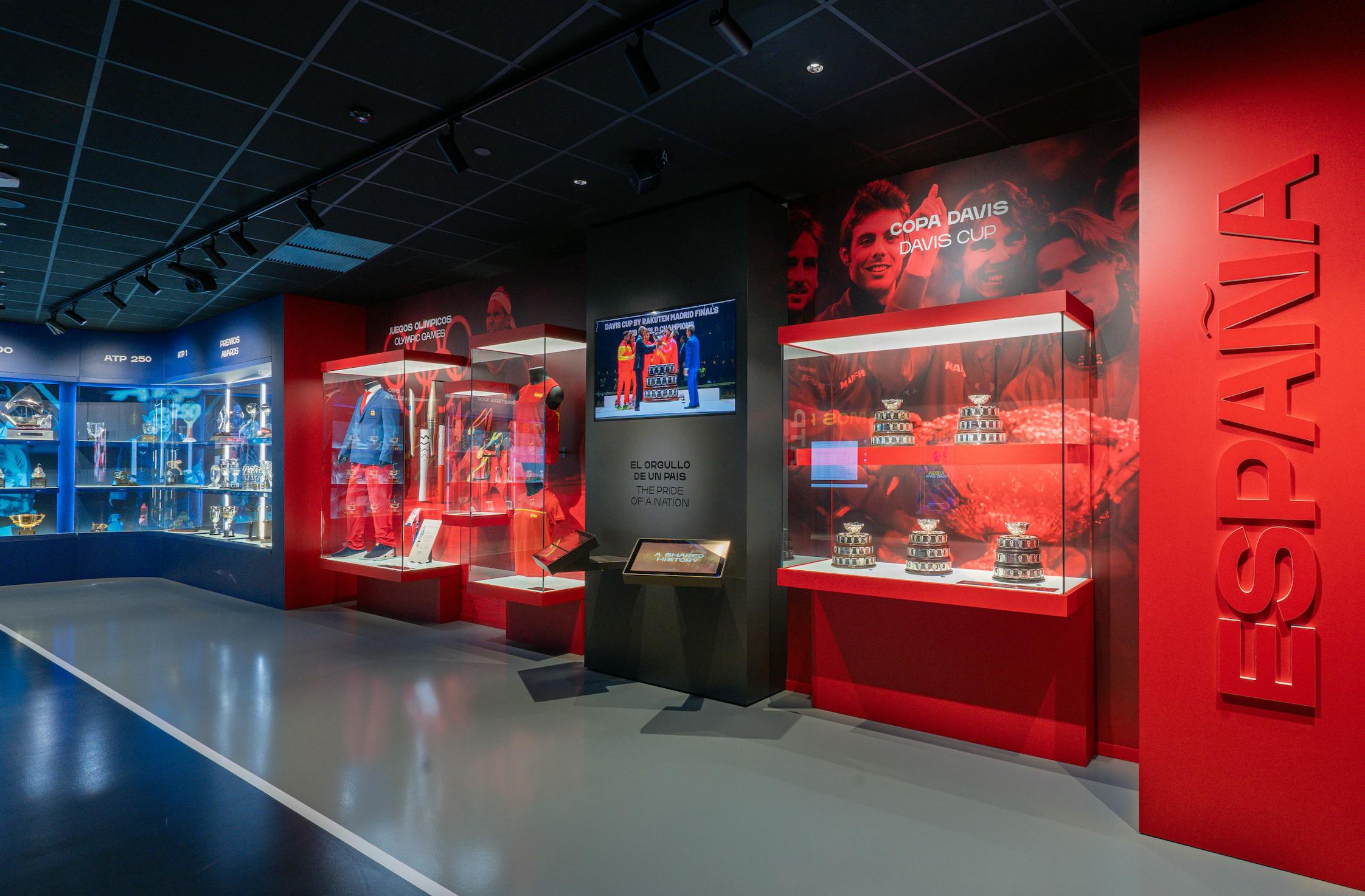 Una exposición que muestra los logros de España en la Copa Davis, con trofeos, fotos y un atrevido diseño rojo con la palabra "España".