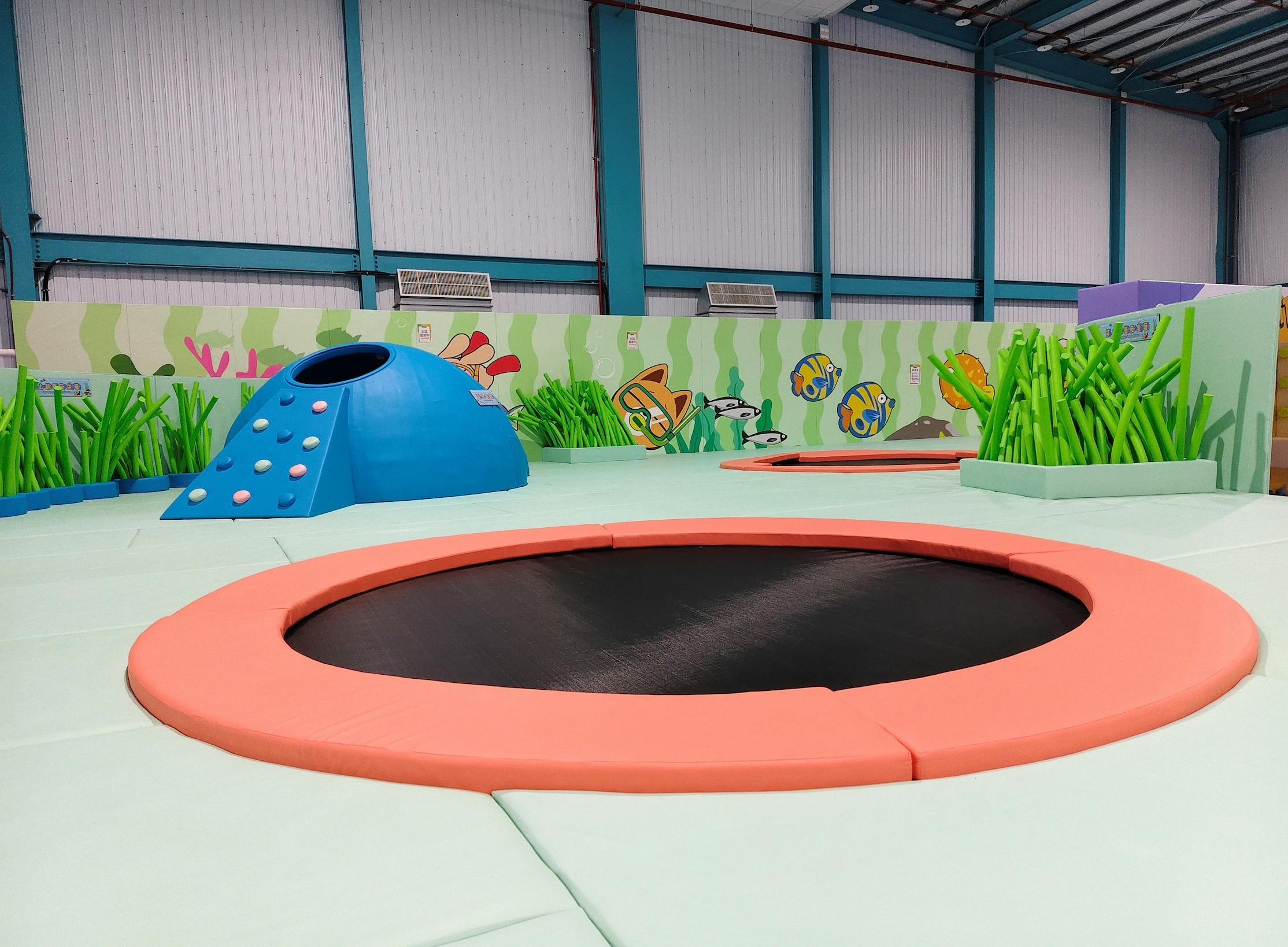 Indoor play area with trampolines, sea-themed decor, and a blue dome structure, under a high-ceilinged roof.