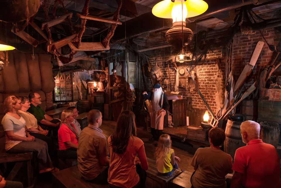 People seated on wooden benches watching a historical reenactment in a dimly lit room with brick walls and rustic decor.