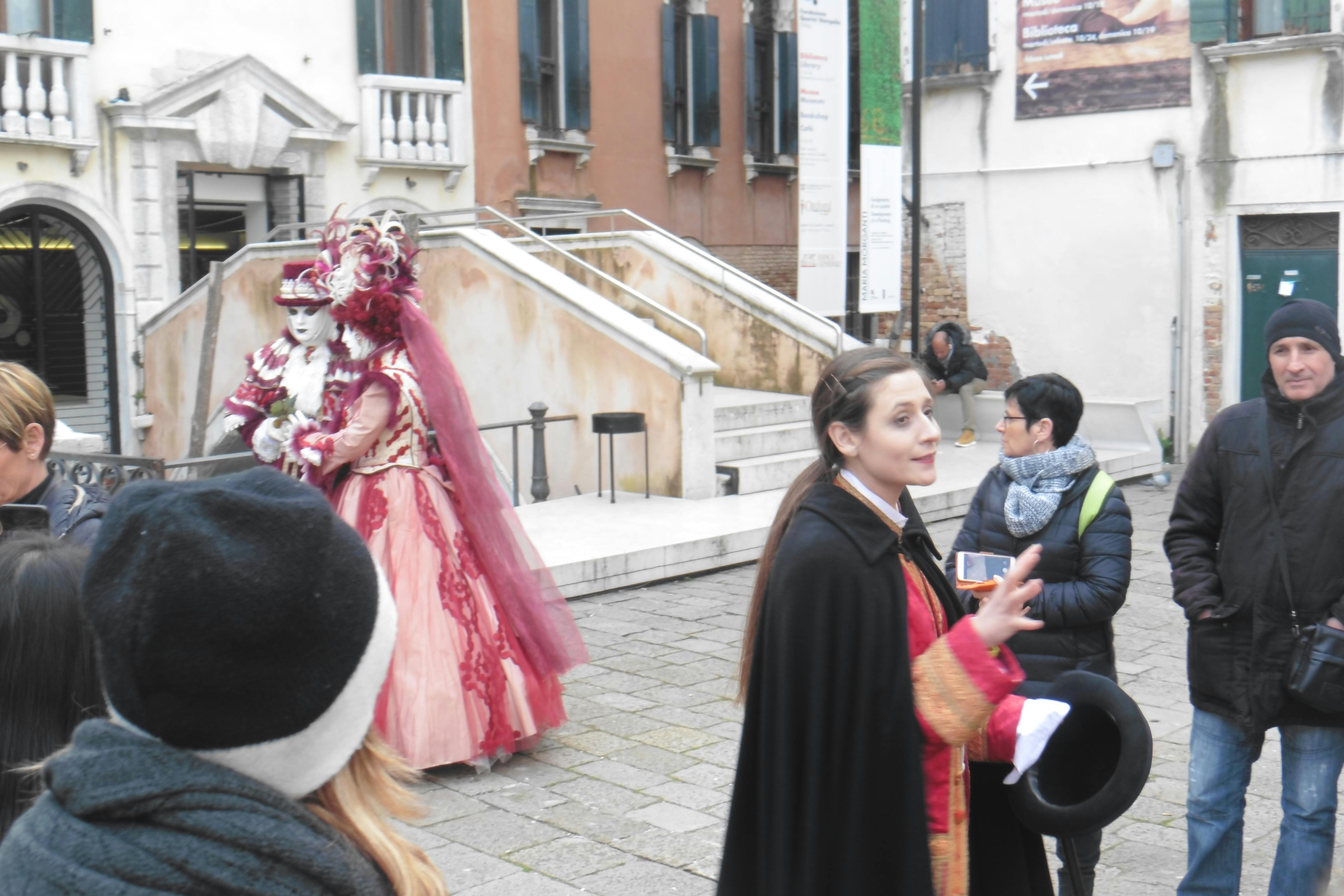 歴史的な衣服を着た女性が3人の人と話しながらジェスチャーをしています。そのうちの1人が写真を撮っています。