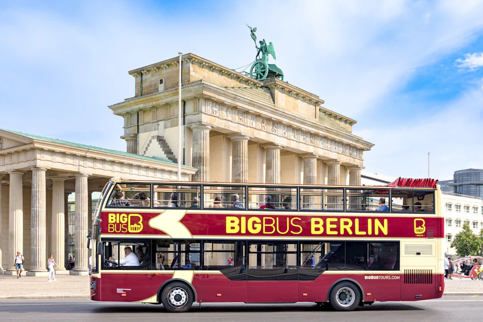 A red double-decker tour bus labeled 'Big Bus Berlin' in front of the Brandenburg Gate under a blue sky.