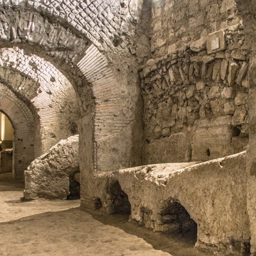 Ancient stone and brick archways and walls of a dimly lit, underground ruin or historic site with rough surfaces and vaulted ceilings.
