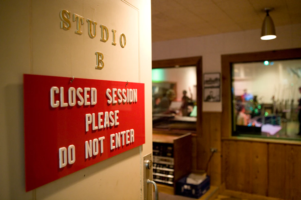 Door labeled "Studio B" with a sign stating "Closed Session Please Do Not Enter." People are visible through a window inside.