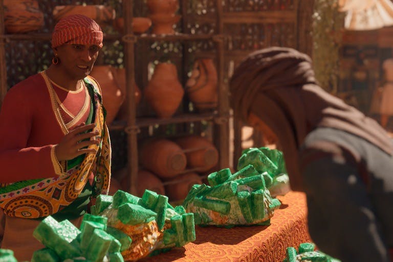 Una persona in abiti colorati sta dietro a un tavolo con rocce minerali verdi, con ceramiche esposte su scaffali sullo sfondo.