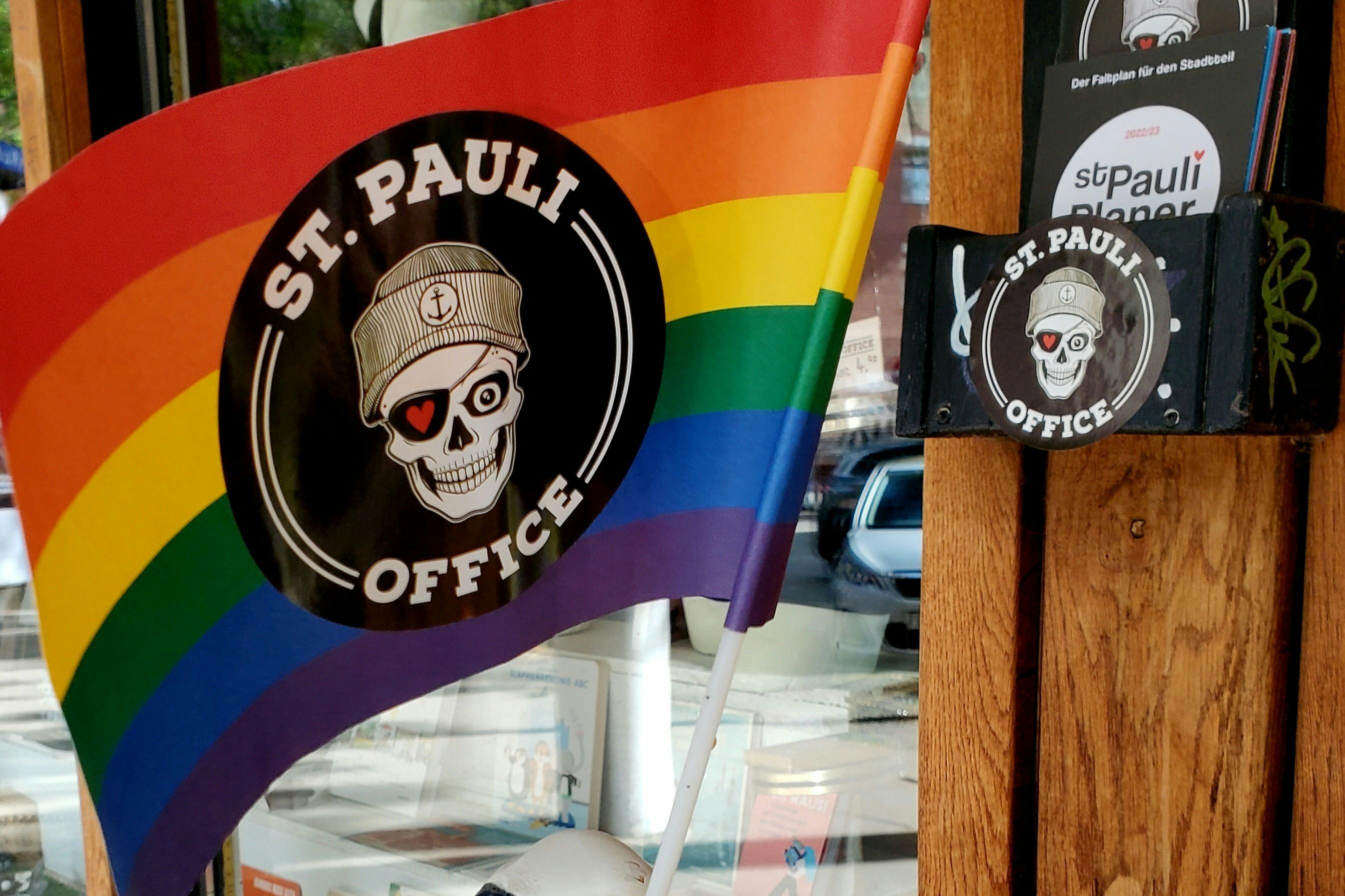 Et regnbueflag med "St. Pauli Office" og et kranium iført en hue i en cirkel i midten.