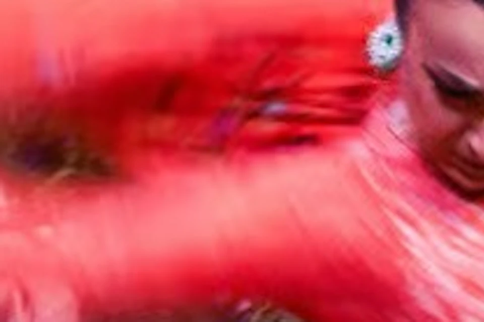 A dancer in a red dress performing energetically, with a blurred motion effect of the dress and background details.