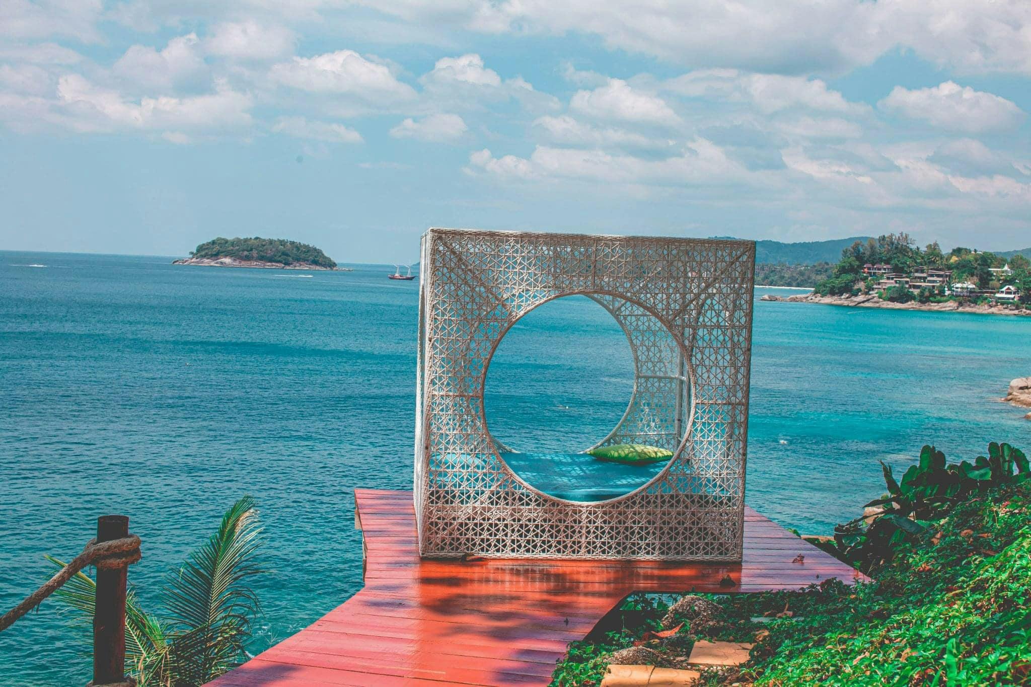 Ornate metallic structure with a circular window, overlooking an ocean with distant islands under a partly cloudy sky.