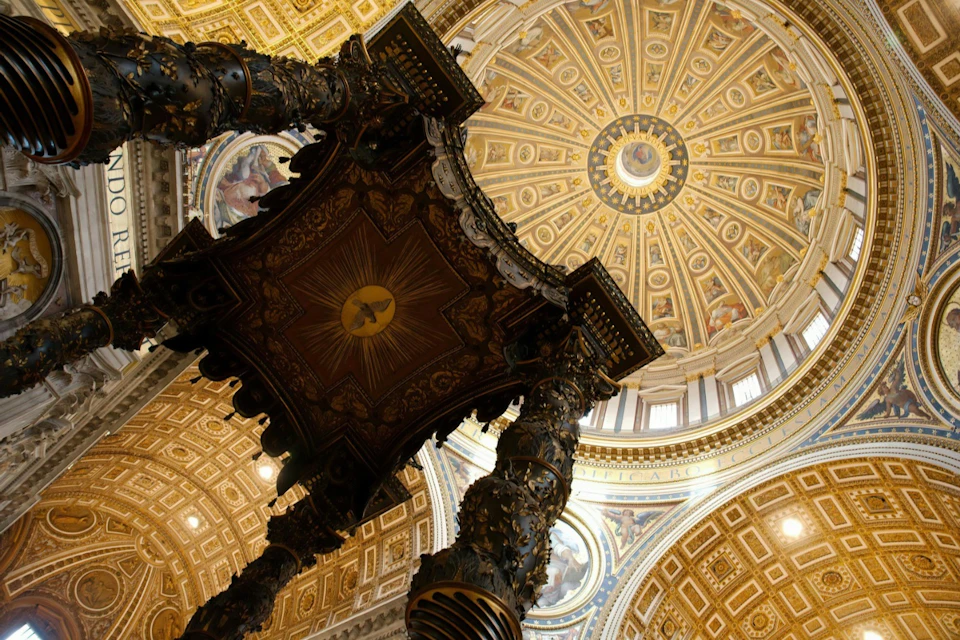Ornate interior of a domed cathedral with a decorative canopy and richly detailed ceiling.