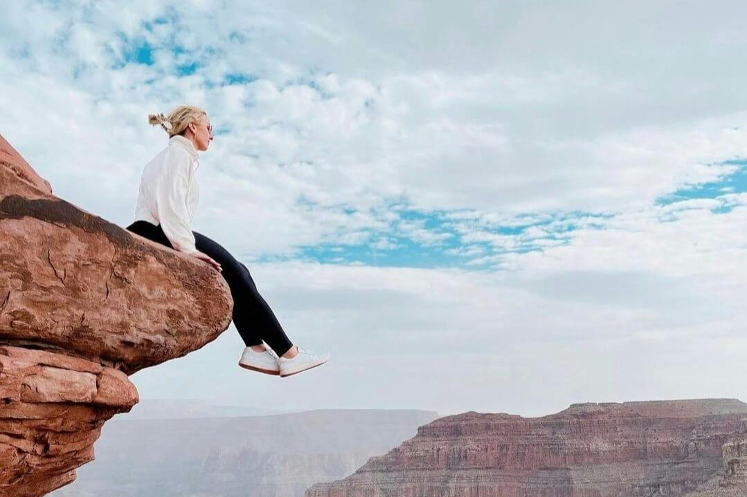 Person sitting on a rock ledge overlooking a canyon under a partly cloudy sky.