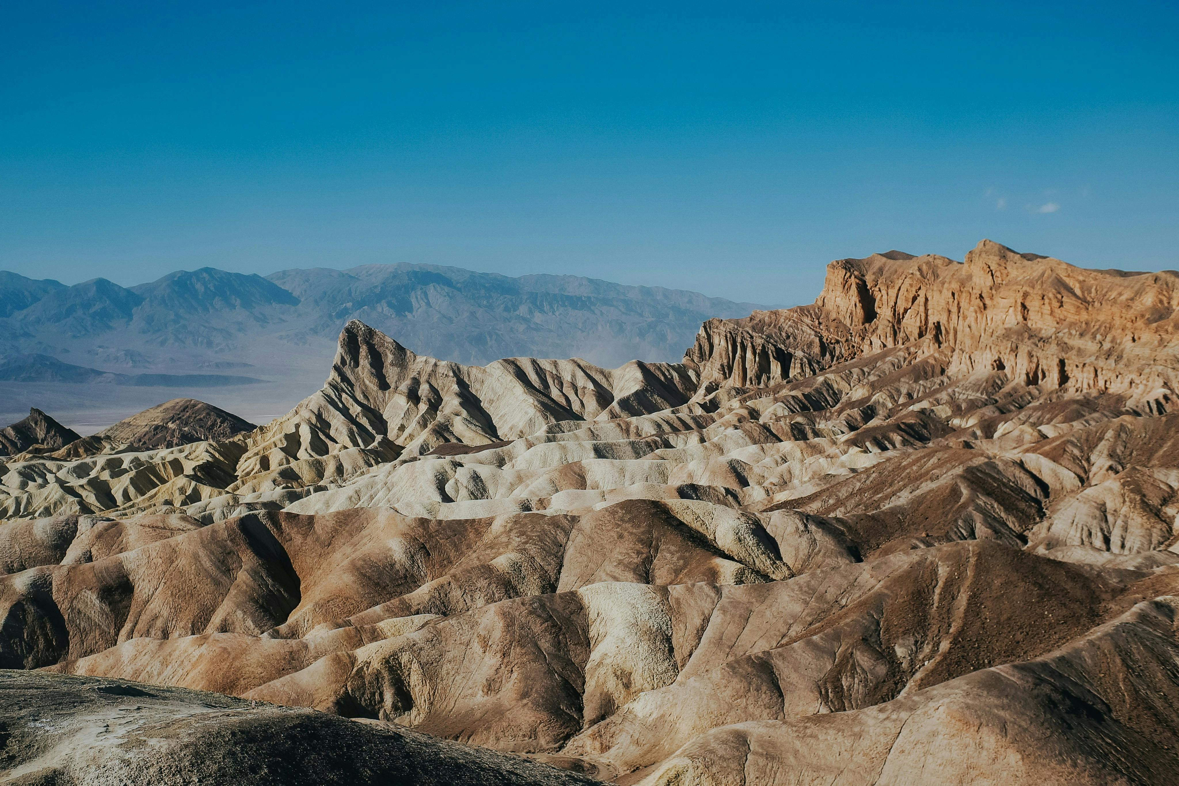 Layered rock formations in a desert landscape under a clear blue sky, with distant mountains in the background.