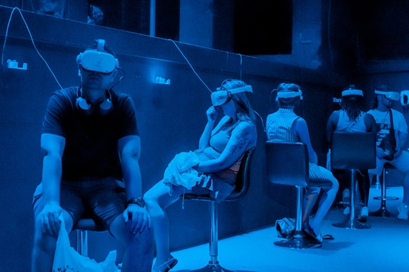 Personer som sitter på stolar med VR-headset i ett svagt upplyst rum med blå belysning.