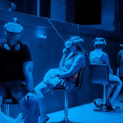 Personer som sitter på stolar med VR-headset i ett svagt upplyst rum med blå belysning.