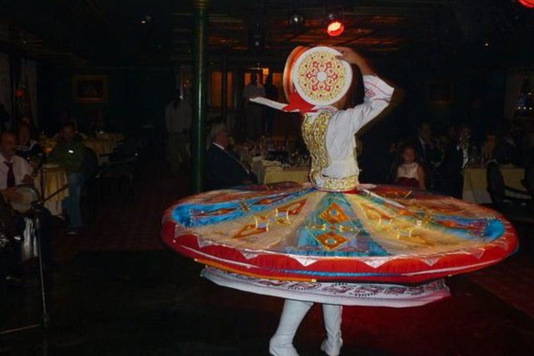 薄暗い部屋で、複雑なパターンのカラフルで広い円形のスカートを着て、伝統的な服装のダンサーがスピンします。