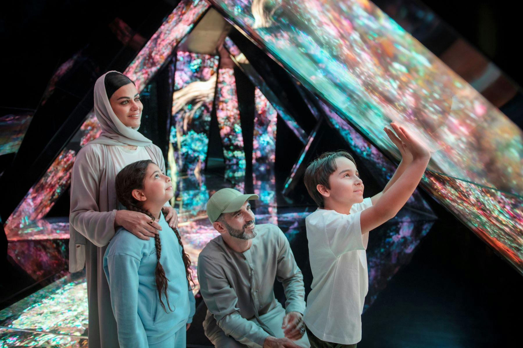 4인 가족은 반사 표면과 빛나는 패턴이 있는 인터랙티브하고 다채로운 전시를 즐길 수 있습니다.