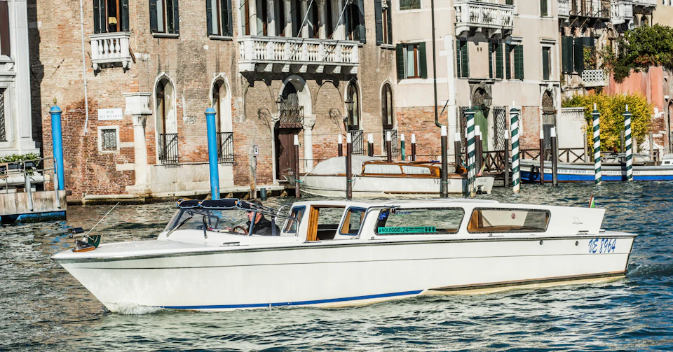 A white motorboat cruises along a canal in front of historic buildings with arched windows and doors.